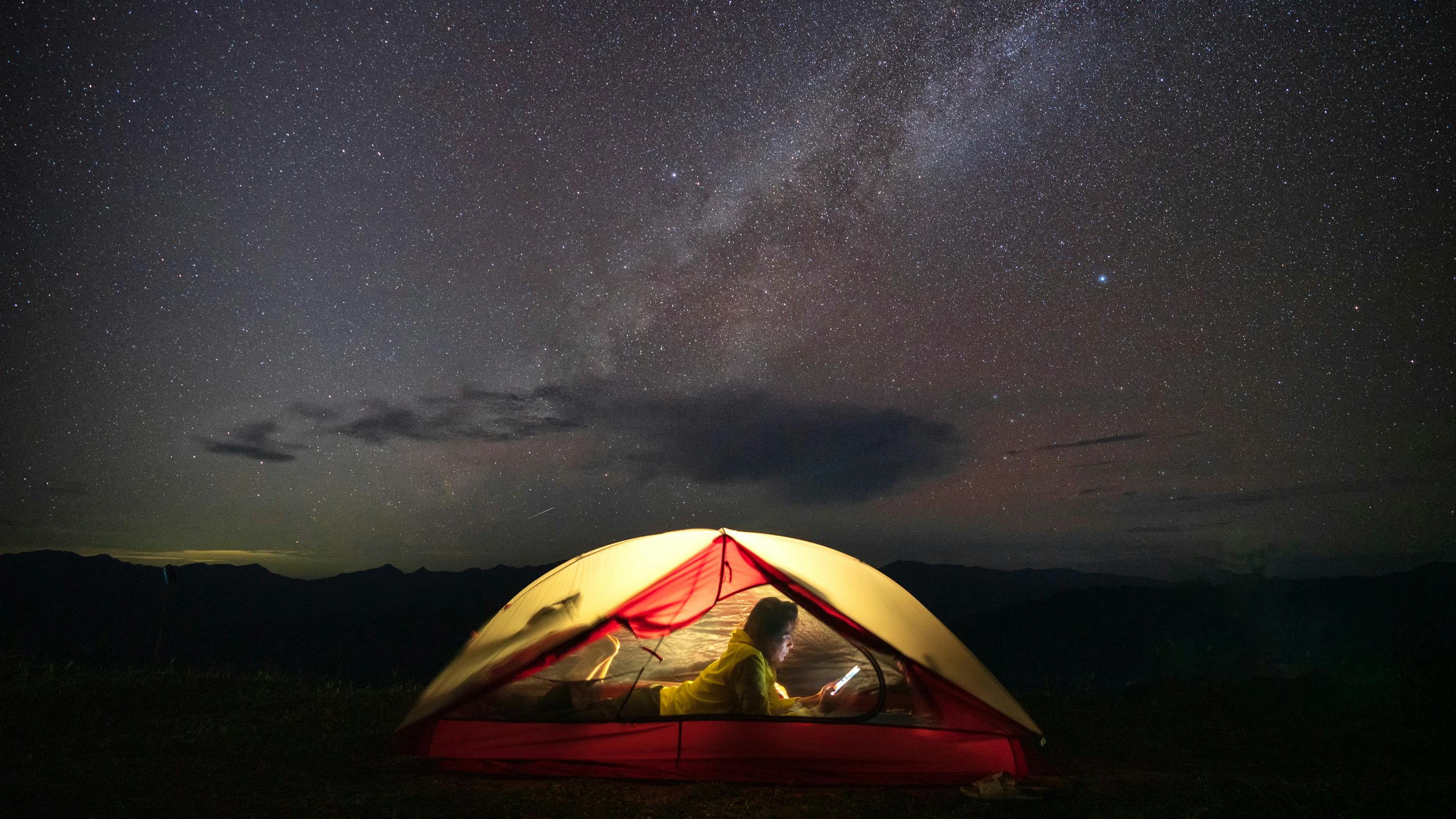 Someone laying in a tent using a smartphone against a starry sky